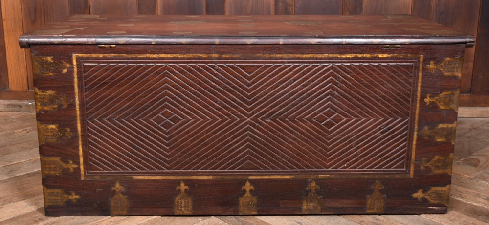 A dark reddish brown padouk wood storage chest featuring a relief-carved floral front panel and decorative brass metal mounts across the top lid and frame. View XIX