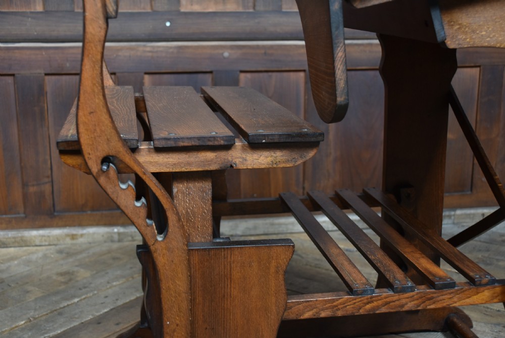 An antique Edwardian oak school desk featuring a slanted writing top, an attached slatted seat, lower shelf slats, and geometric marquetry inlay on the side panel. View VI