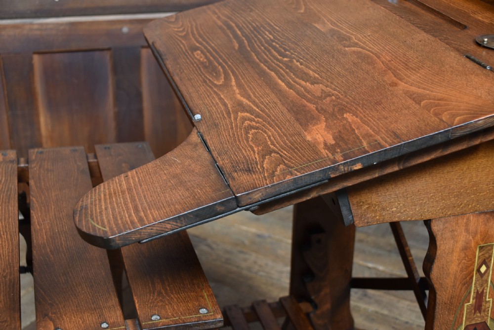 An antique Edwardian oak school desk featuring a slanted writing top, an attached slatted seat, lower shelf slats, and geometric marquetry inlay on the side panel. View XIII