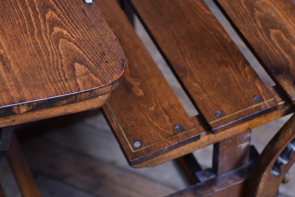 An antique Edwardian oak school desk featuring a slanted writing top, an attached slatted seat, lower shelf slats, and geometric marquetry inlay on the side panel. View XIX