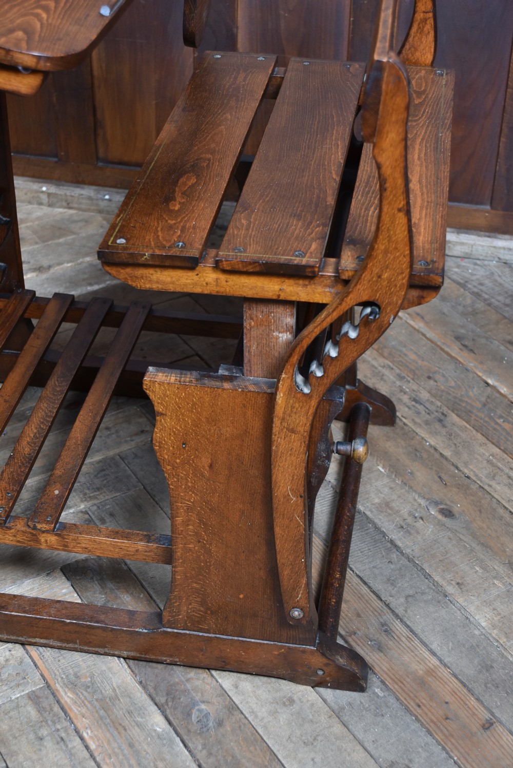 An antique Edwardian oak school desk featuring a slanted writing top, an attached slatted seat, lower shelf slats, and geometric marquetry inlay on the side panel. View XX