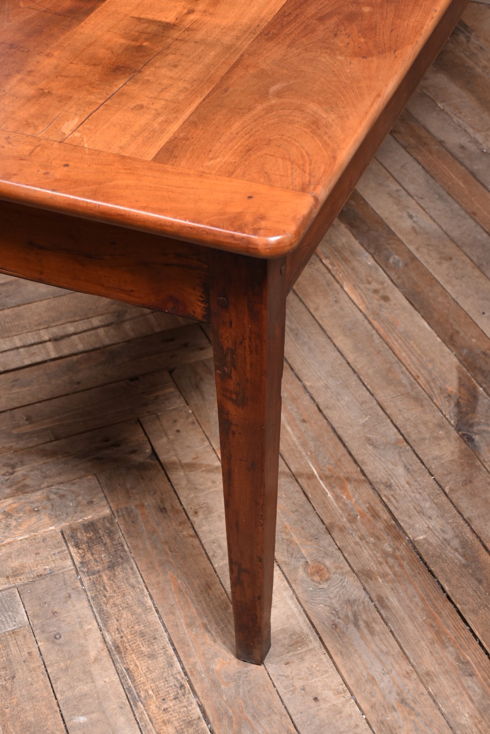 A long antique French cherry wood farmhouse table featuring tapered legs, a single side drawer with a metal cup handle, and a plank top with framed borders. View VI