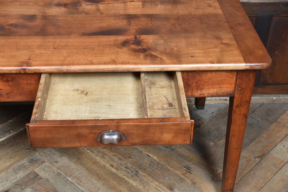 A long antique French cherry wood farmhouse table featuring tapered legs, a single side drawer with a metal cup handle, and a plank top with framed borders. View X