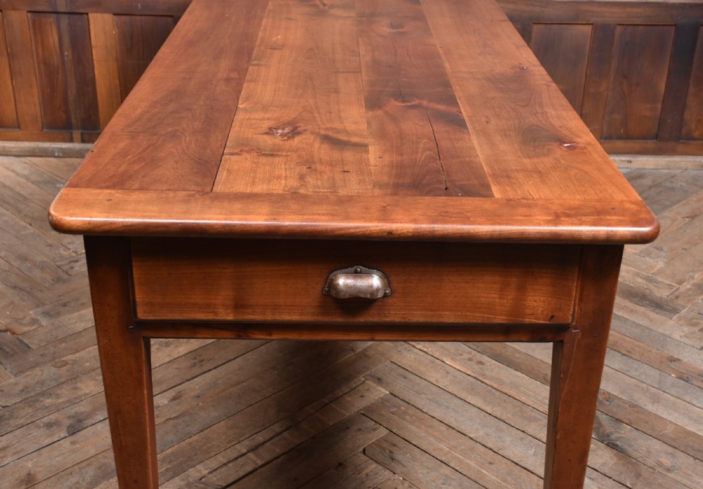 A long antique French cherry wood farmhouse table featuring tapered legs, a single side drawer with a metal cup handle, and a plank top with framed borders. View XII