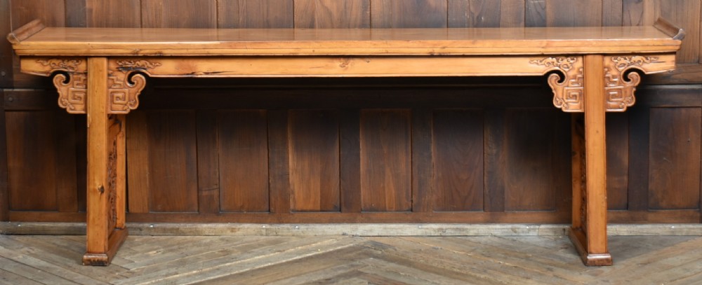 A long, light honey brown timber Chinese altar console table featuring upturned flange ends and carved decorative spandrels.