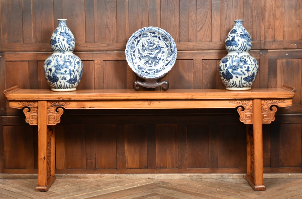 A long, light honey brown timber Chinese altar console table featuring upturned flange ends and carved decorative spandrels. View II