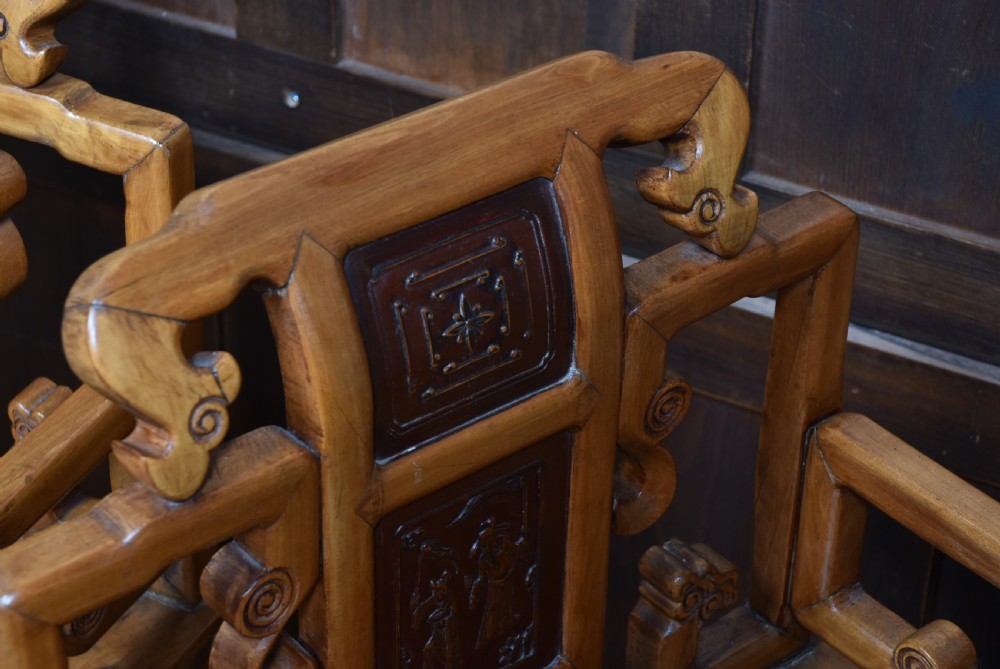 A pair of carved Chinese hardwood armchairs featuring decorative splats with darker wood relief panels and openwork arms. View III