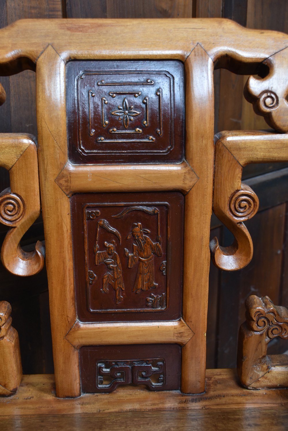 A pair of carved Chinese hardwood armchairs featuring decorative splats with darker wood relief panels and openwork arms. View XV