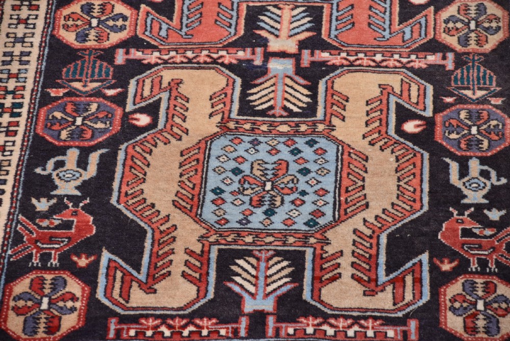 A hand-knotted wool runner rug featuring geometric medallions, bird motifs, and decorative borders in terracotta, cream, blue, and dark navy tones. View VI