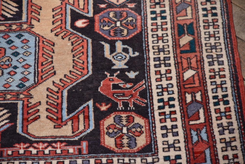 A hand-knotted wool runner rug featuring geometric medallions, bird motifs, and decorative borders in terracotta, cream, blue, and dark navy tones. View VII