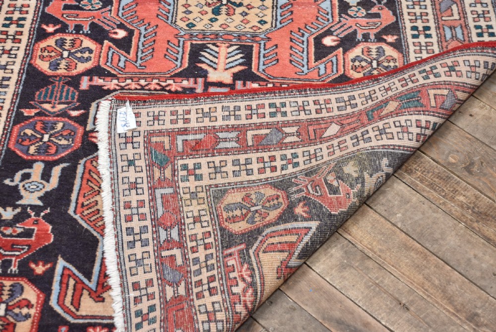 A hand-knotted wool runner rug featuring geometric medallions, bird motifs, and decorative borders in terracotta, cream, blue, and dark navy tones. View X