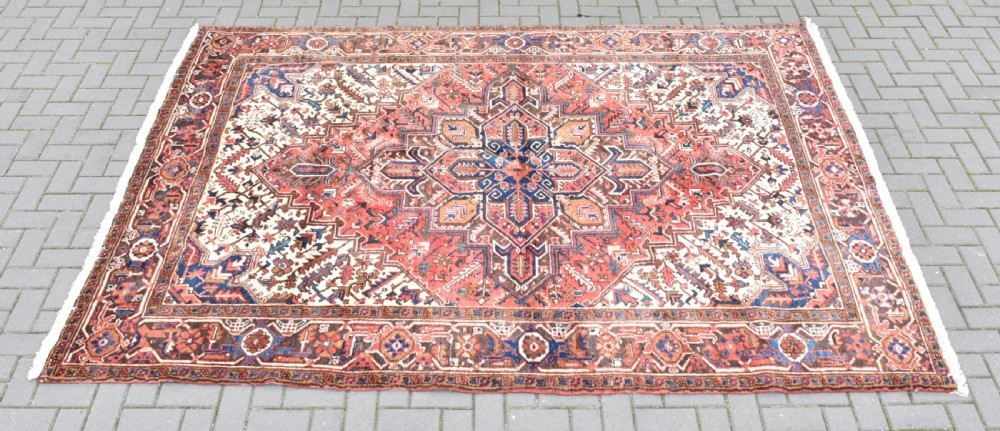 A rectangular hand-knotted Persian wool rug featuring a large geometric central medallion in navy and terracotta over a cream field with patterned borders.
