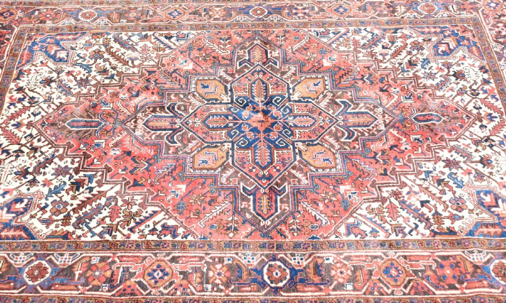 A rectangular hand-knotted Persian wool rug featuring a large geometric central medallion in navy and terracotta over a cream field with patterned borders. View II