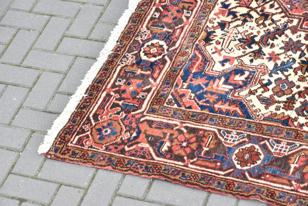 A rectangular hand-knotted Persian wool rug featuring a large geometric central medallion in navy and terracotta over a cream field with patterned borders. View III
