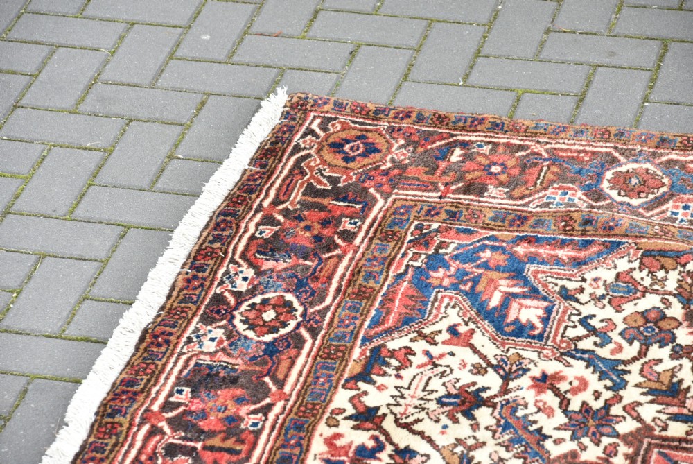A rectangular hand-knotted Persian wool rug featuring a large geometric central medallion in navy and terracotta over a cream field with patterned borders. View IV