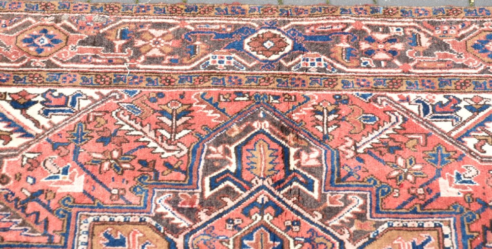 A rectangular hand-knotted Persian wool rug featuring a large geometric central medallion in navy and terracotta over a cream field with patterned borders. View V