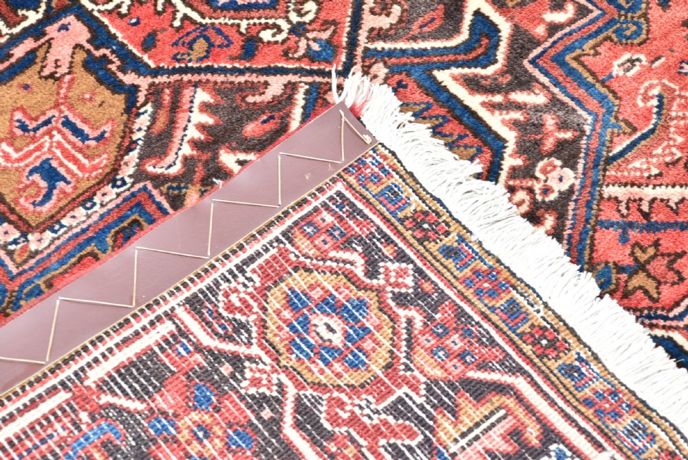 A rectangular hand-knotted Persian wool rug featuring a large geometric central medallion in navy and terracotta over a cream field with patterned borders. View X