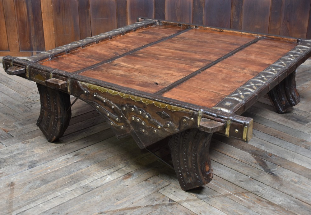 A low square coffee table crafted from a dark reclaimed bullock cart frame with decorative brass studding and stout carved legs. View II
