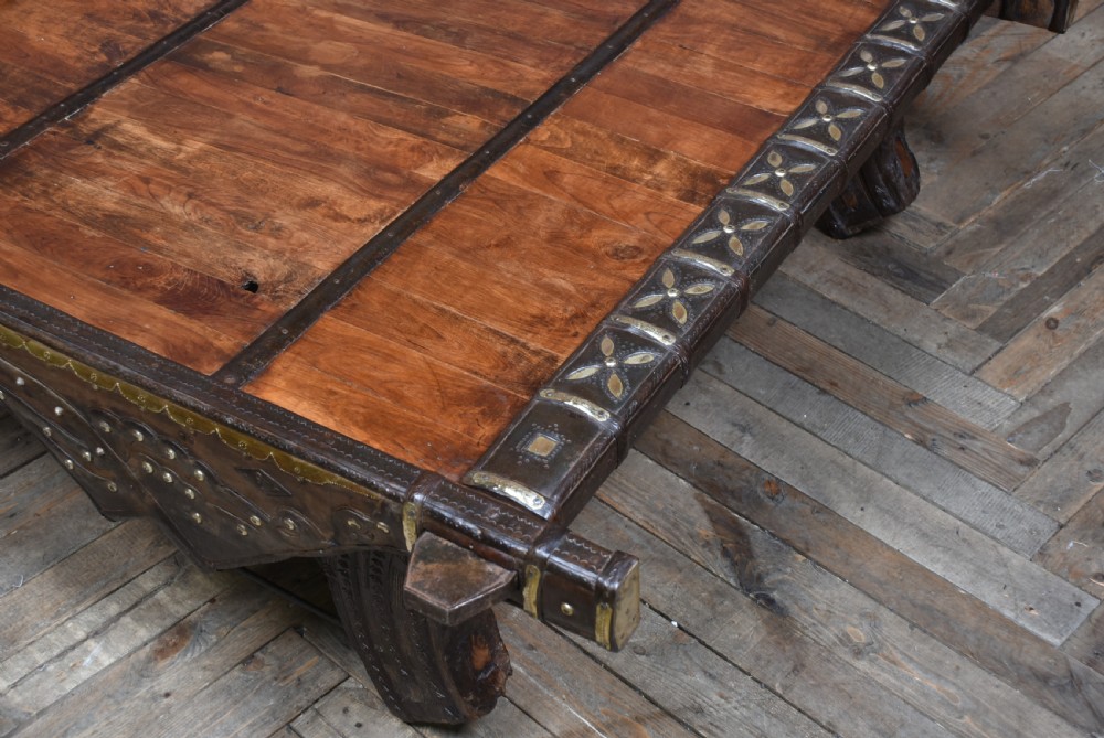 A low square coffee table crafted from a dark reclaimed bullock cart frame with decorative brass studding and stout carved legs. View III
