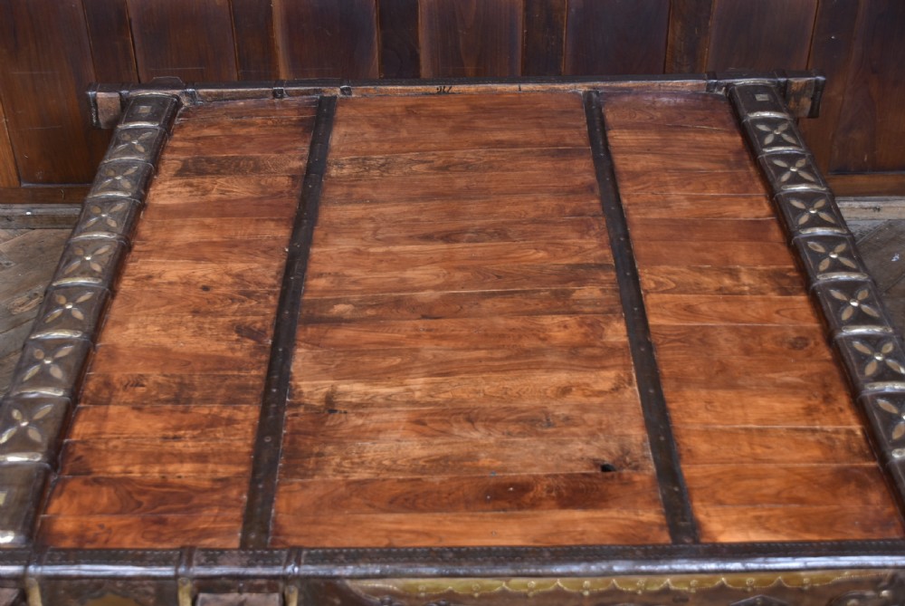 A low square coffee table crafted from a dark reclaimed bullock cart frame with decorative brass studding and stout carved legs. View VII