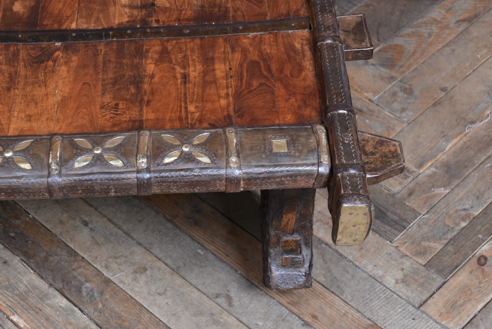 A low square coffee table crafted from a dark reclaimed bullock cart frame with decorative brass studding and stout carved legs. View XI