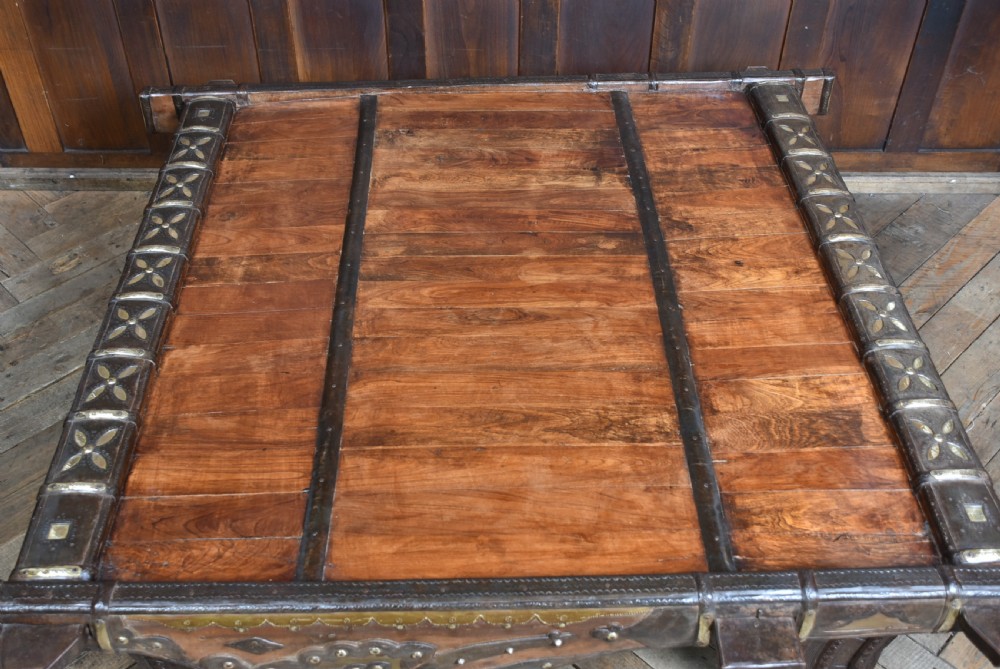 A low square coffee table crafted from a dark reclaimed bullock cart frame with decorative brass studding and stout carved legs. View XIV