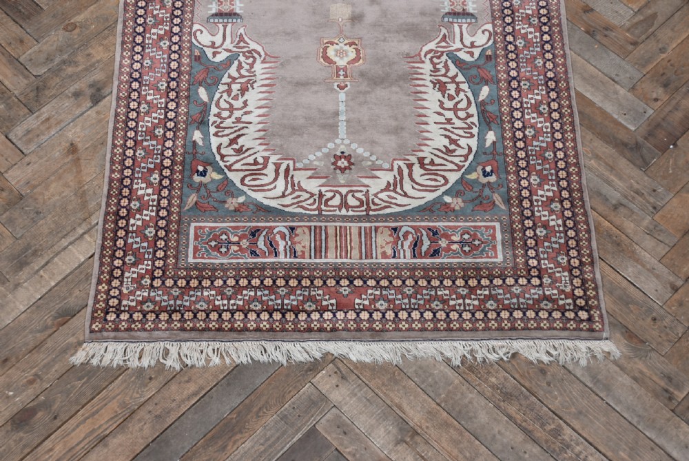 A hand-woven silk prayer rug featuring a central arched mihrab motif in taupe, framed by intricate terracotta and slate blue geometric floral borders with fringe at both ends. View III