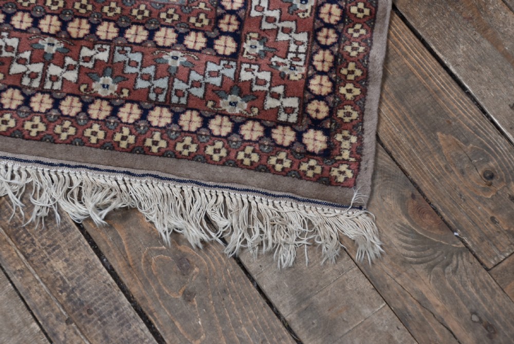 A hand-woven silk prayer rug featuring a central arched mihrab motif in taupe, framed by intricate terracotta and slate blue geometric floral borders with fringe at both ends. View VI