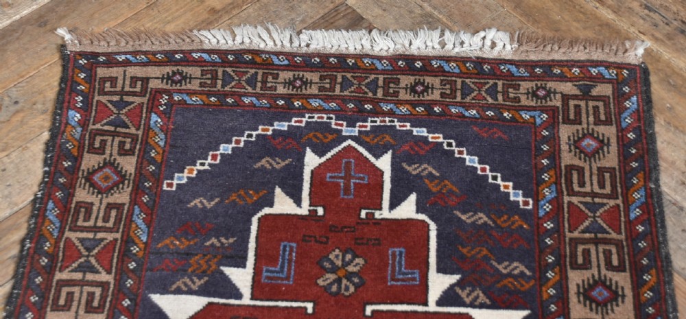 A hand-knotted vintage Oriental wool rug featuring geometric stepped medallions in terracotta red and cream set against a dark navy blue field with detailed tribal borders. View III