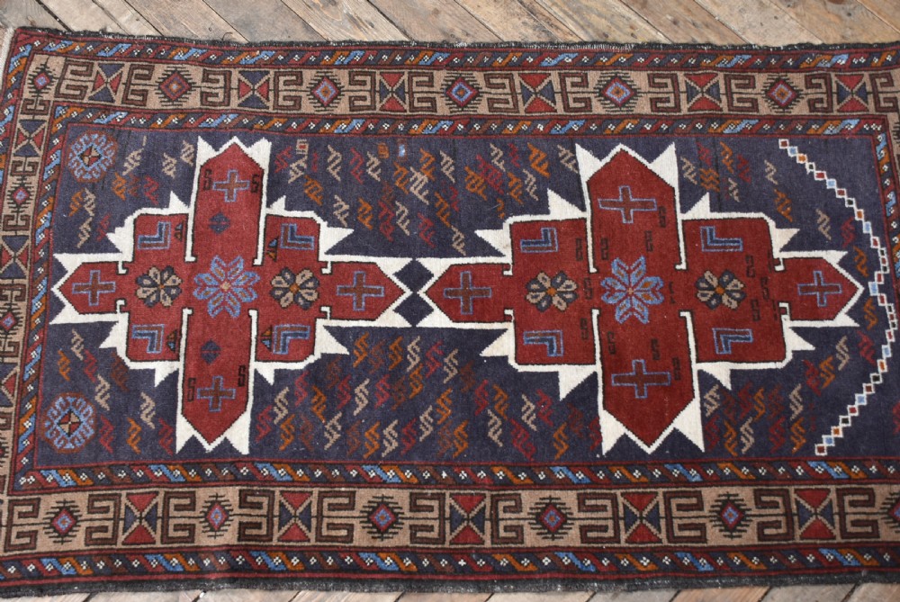 A hand-knotted vintage Oriental wool rug featuring geometric stepped medallions in terracotta red and cream set against a dark navy blue field with detailed tribal borders. View V