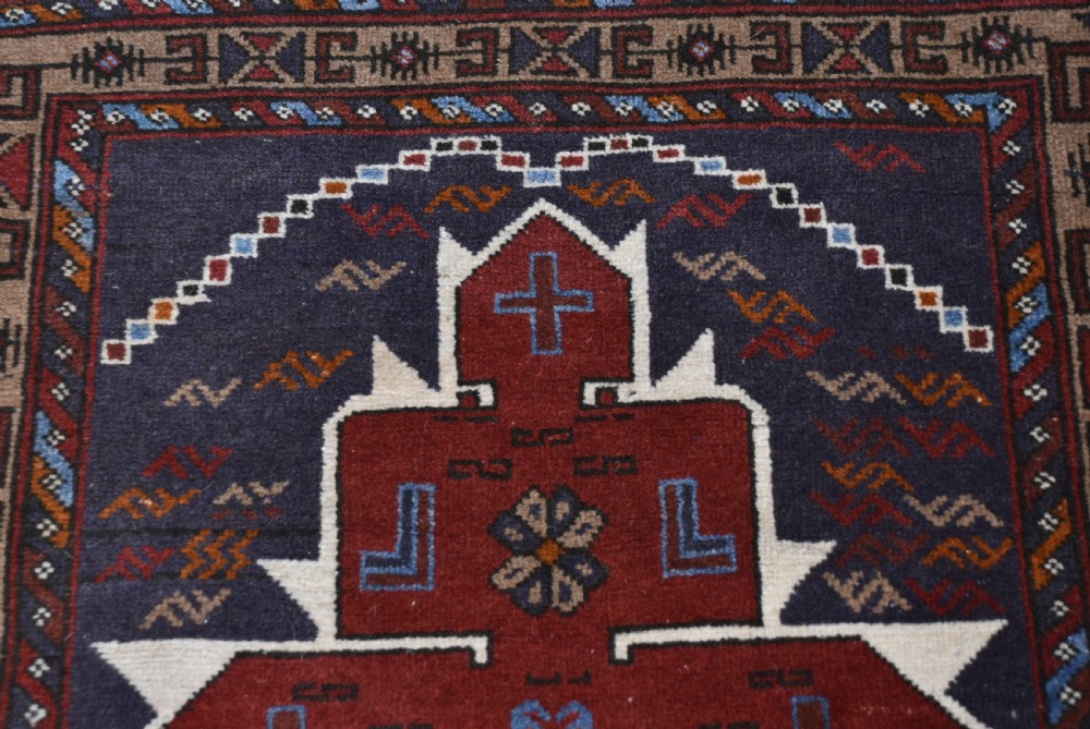 A hand-knotted vintage Oriental wool rug featuring geometric stepped medallions in terracotta red and cream set against a dark navy blue field with detailed tribal borders. View VI