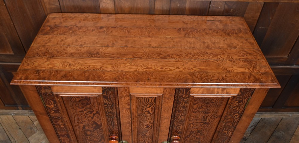 A Victorian Hungarian ash cupboard featuring highly figured swirling veneer panels, turned wooden knobs, brass keyhole escutcheons, and a solid plinth base. View III