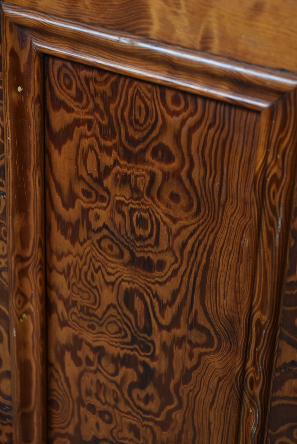A Victorian Hungarian ash cupboard featuring highly figured swirling veneer panels, turned wooden knobs, brass keyhole escutcheons, and a solid plinth base. View VII