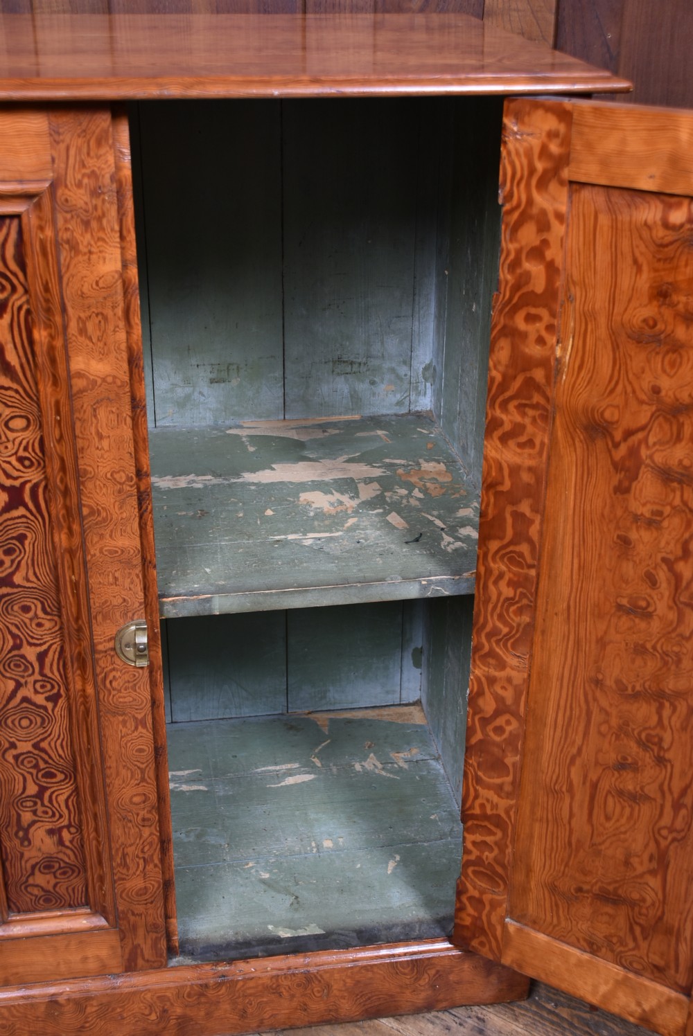 A Victorian Hungarian ash cupboard featuring highly figured swirling veneer panels, turned wooden knobs, brass keyhole escutcheons, and a solid plinth base. View X