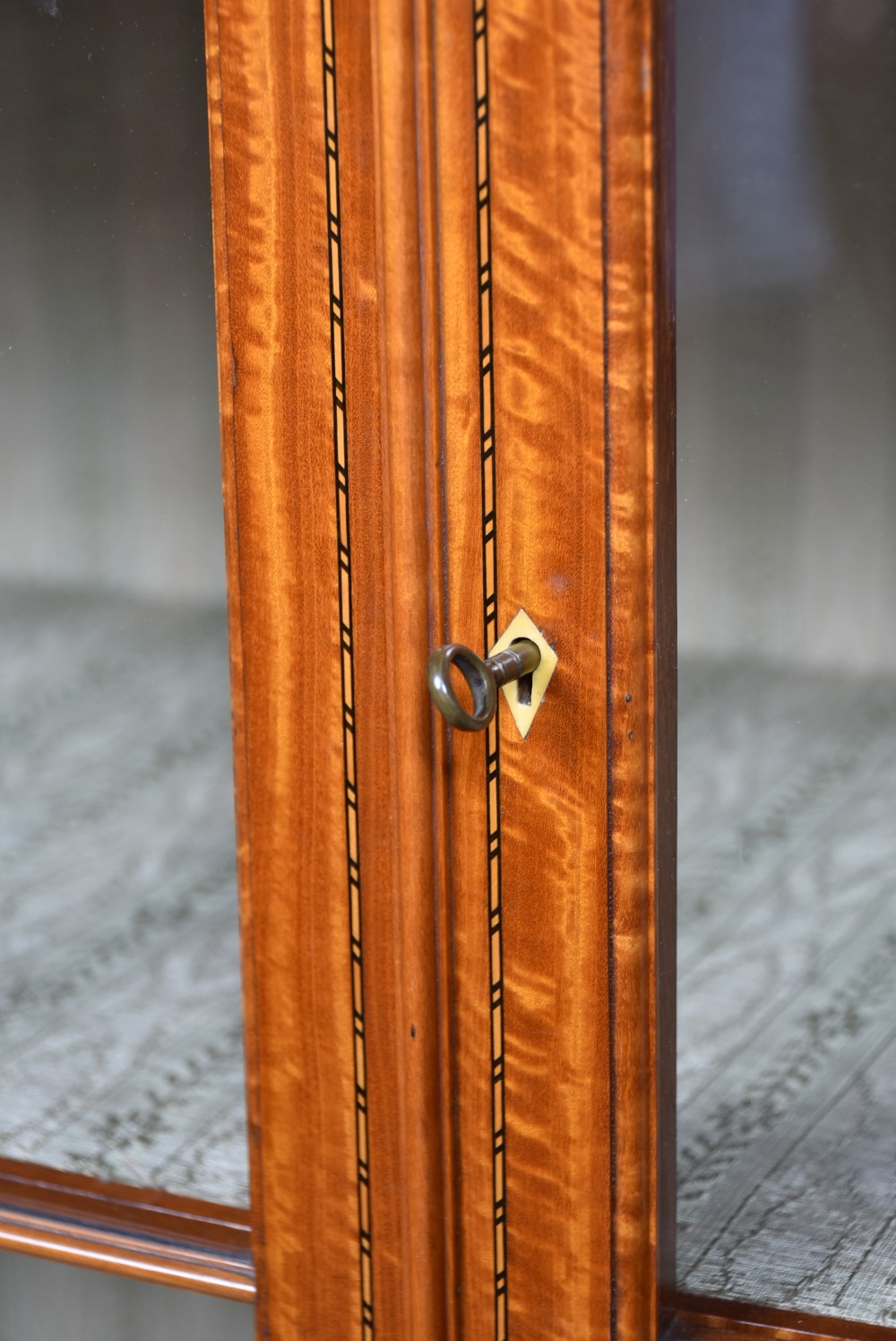 An Edwardian satinwood display cabinet with two glazed upper doors, two chevron veneer lower doors, and tapered square legs with an open undershelf. View VII