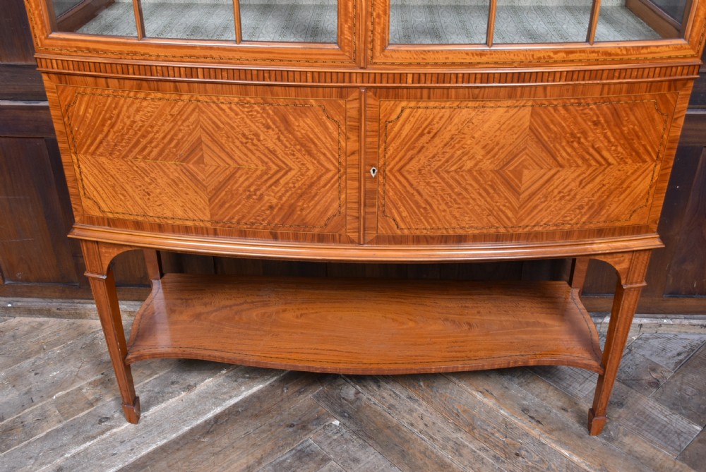 An Edwardian satinwood display cabinet with two glazed upper doors, two chevron veneer lower doors, and tapered square legs with an open undershelf. View VIII