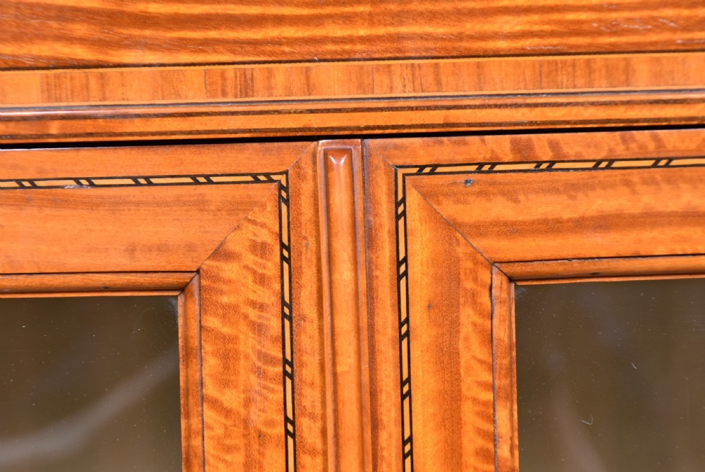 An Edwardian satinwood display cabinet with two glazed upper doors, two chevron veneer lower doors, and tapered square legs with an open undershelf. View X