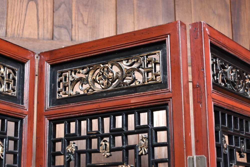 A four-panel tall folding room screen featuring red-lacquered timber framing, intricate black lattice fretwork, and carved gilded lower panels. View II