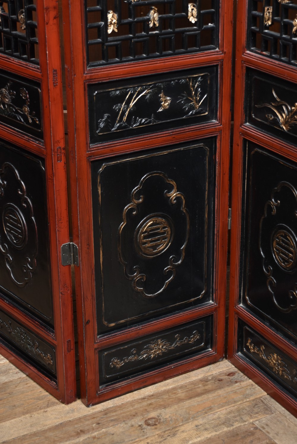 A four-panel tall folding room screen featuring red-lacquered timber framing, intricate black lattice fretwork, and carved gilded lower panels. View VI