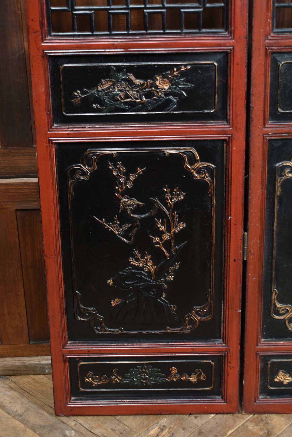 A four-panel tall folding room screen featuring red-lacquered timber framing, intricate black lattice fretwork, and carved gilded lower panels. View IX