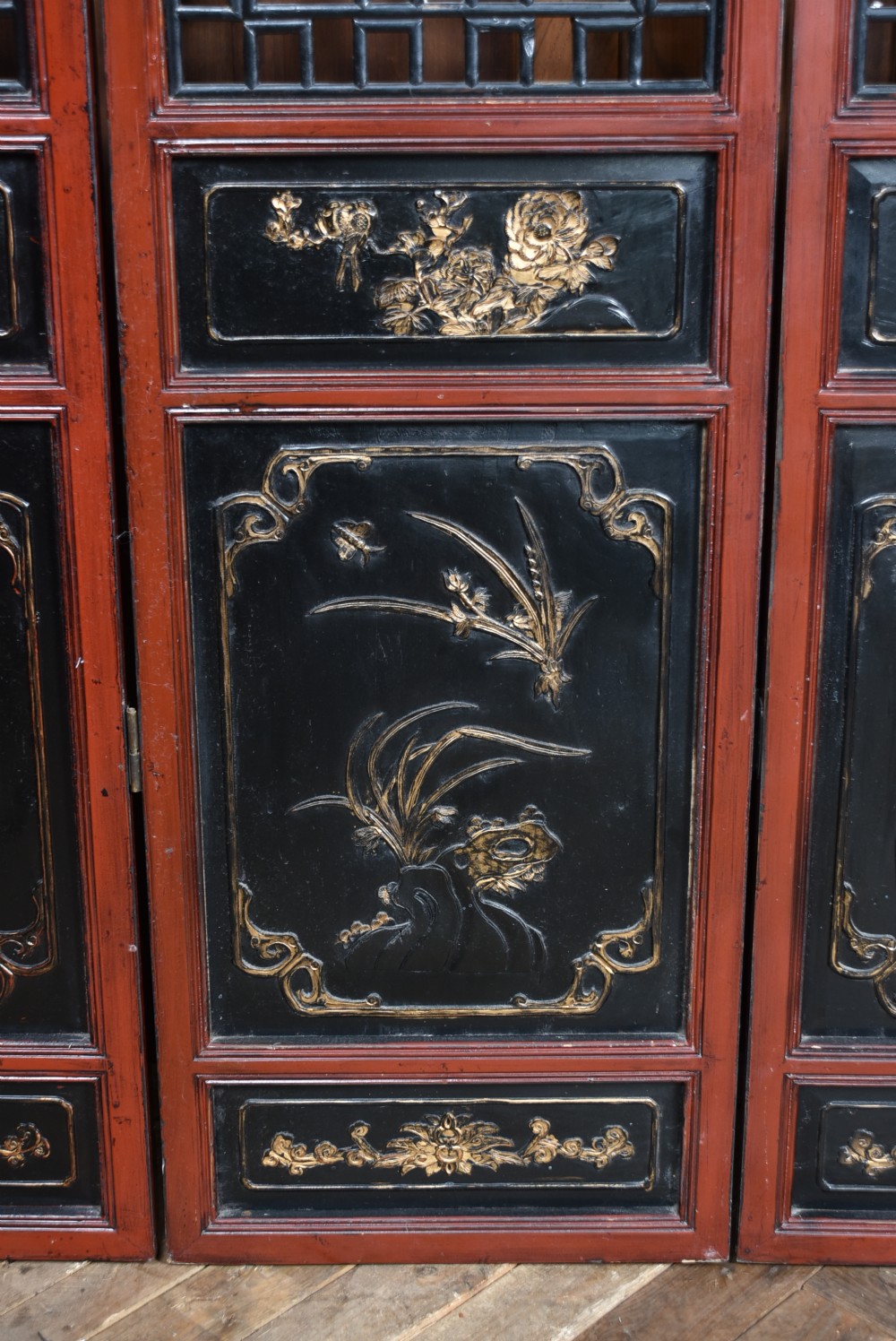 A four-panel tall folding room screen featuring red-lacquered timber framing, intricate black lattice fretwork, and carved gilded lower panels. View X