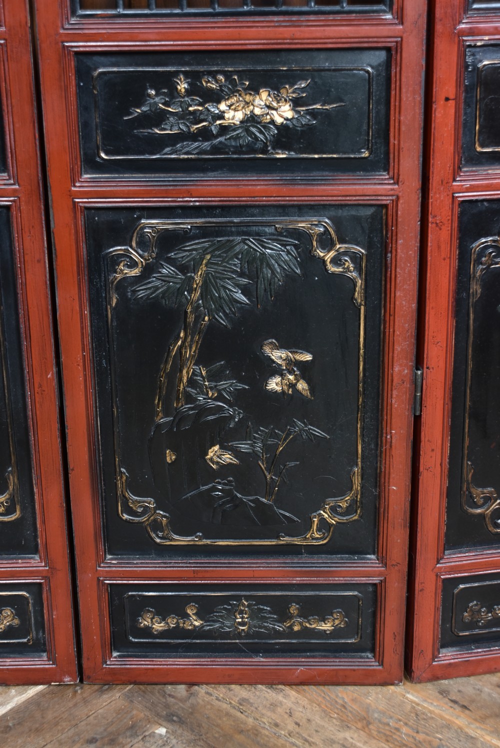 A four-panel tall folding room screen featuring red-lacquered timber framing, intricate black lattice fretwork, and carved gilded lower panels. View XI