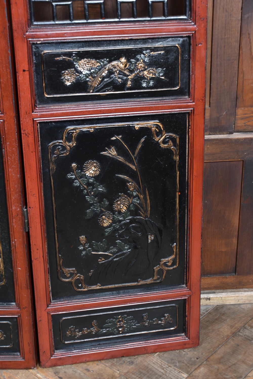 A four-panel tall folding room screen featuring red-lacquered timber framing, intricate black lattice fretwork, and carved gilded lower panels. View XII