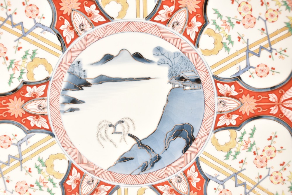 A circular Japanese Imari porcelain charger plate featuring a central landscape roundel surrounded by iron red and cobalt blue floral reserves. View III