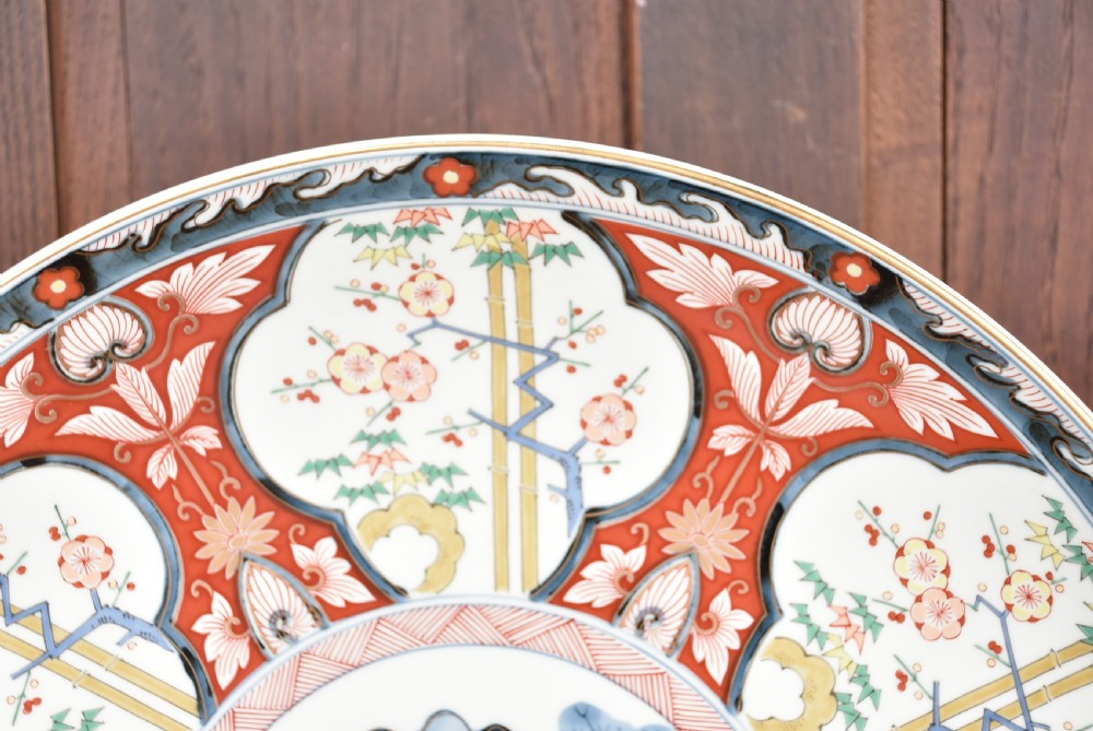 A circular Japanese Imari porcelain charger plate featuring a central landscape roundel surrounded by iron red and cobalt blue floral reserves. View V