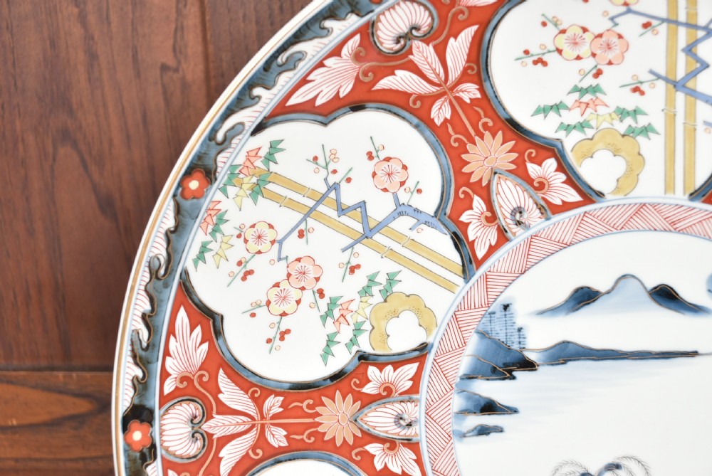 A circular Japanese Imari porcelain charger plate featuring a central landscape roundel surrounded by iron red and cobalt blue floral reserves. View VI