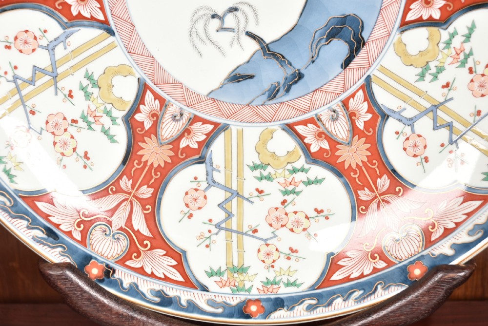 A circular Japanese Imari porcelain charger plate featuring a central landscape roundel surrounded by iron red and cobalt blue floral reserves. View VII