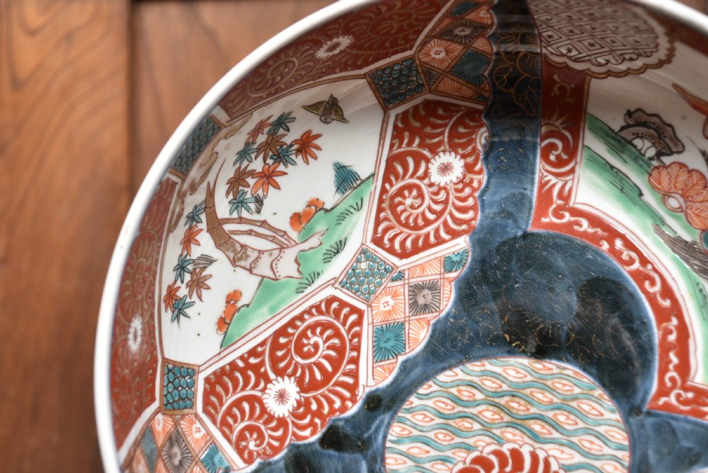A round Japanese Imari porcelain bowl styled with cobalt blue and iron-red panelled decoration, resting on a carved dark wooden display stand. View II