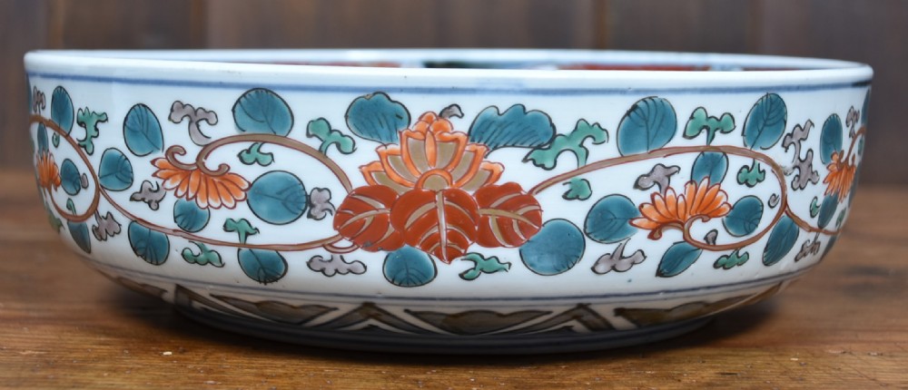 A round Japanese Imari porcelain bowl styled with cobalt blue and iron-red panelled decoration, resting on a carved dark wooden display stand. View IV