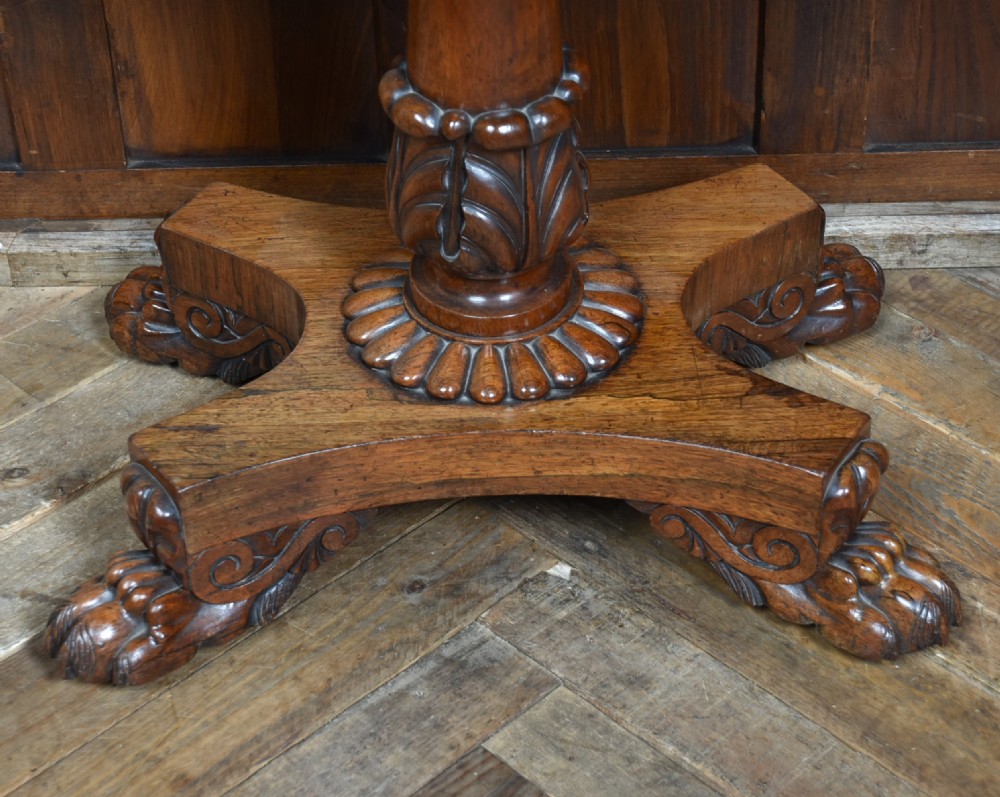 A Victorian rosewood fold-over games table featuring a polished rectangular top, turned carved pedestal stem, and a quadripartite plinth base with carved claw feet. View VI